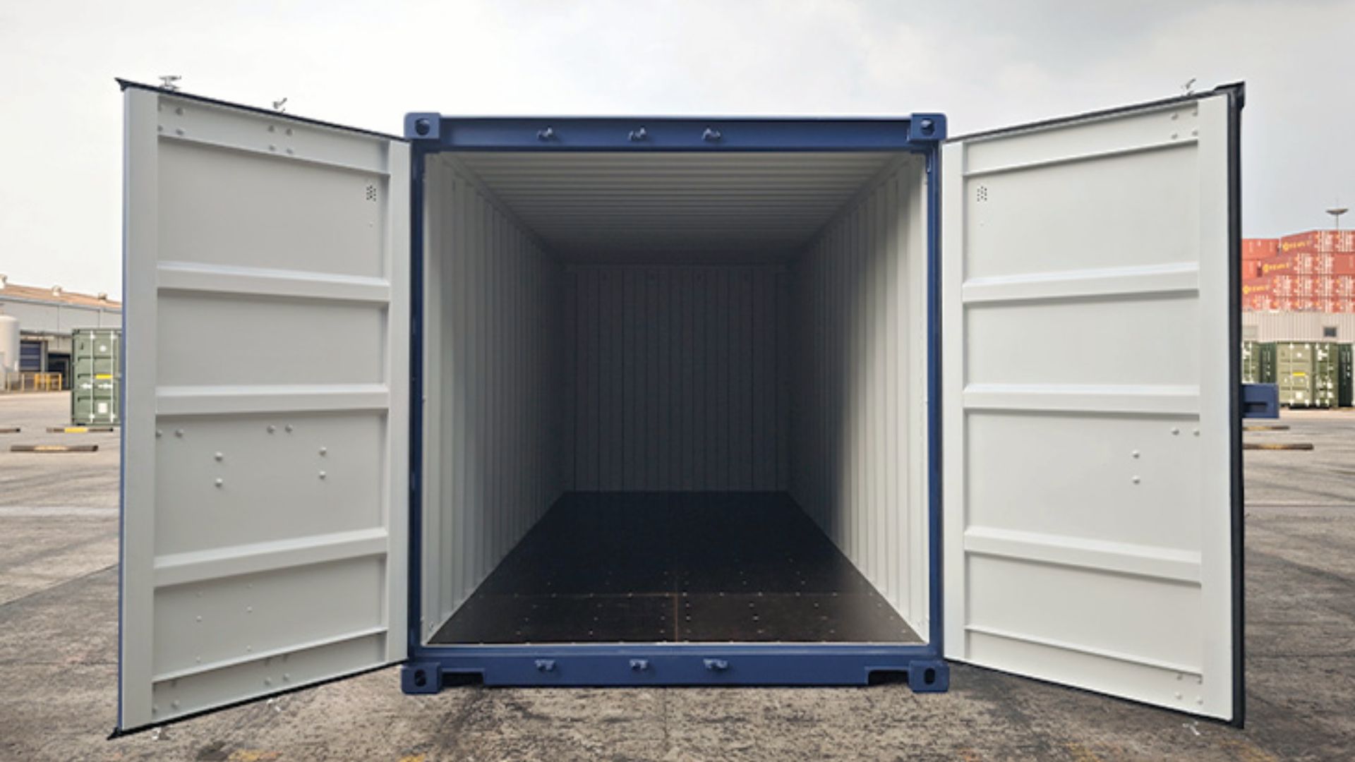 Open empty blue shipping container with both doors wide, showing the interior floor and walls at a depot.