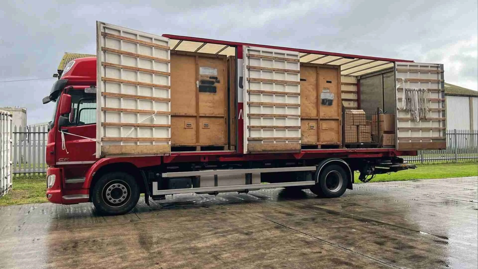 Red moving truck loaded with large wooden crates ready for transport to secure storage warehouse facility