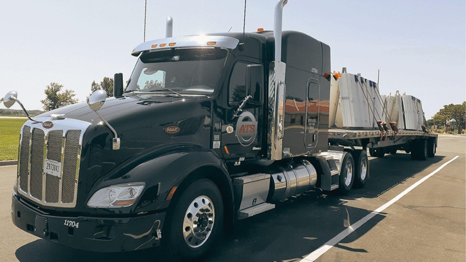 Black ATS semi hauling secured freight on a flatbed trailer under clear skies.