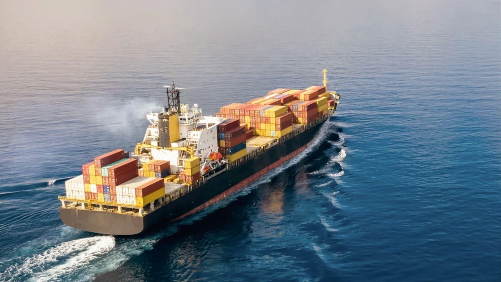 Aerial view of container ship moving through sea, depicting commodity delivery across trade lanes.