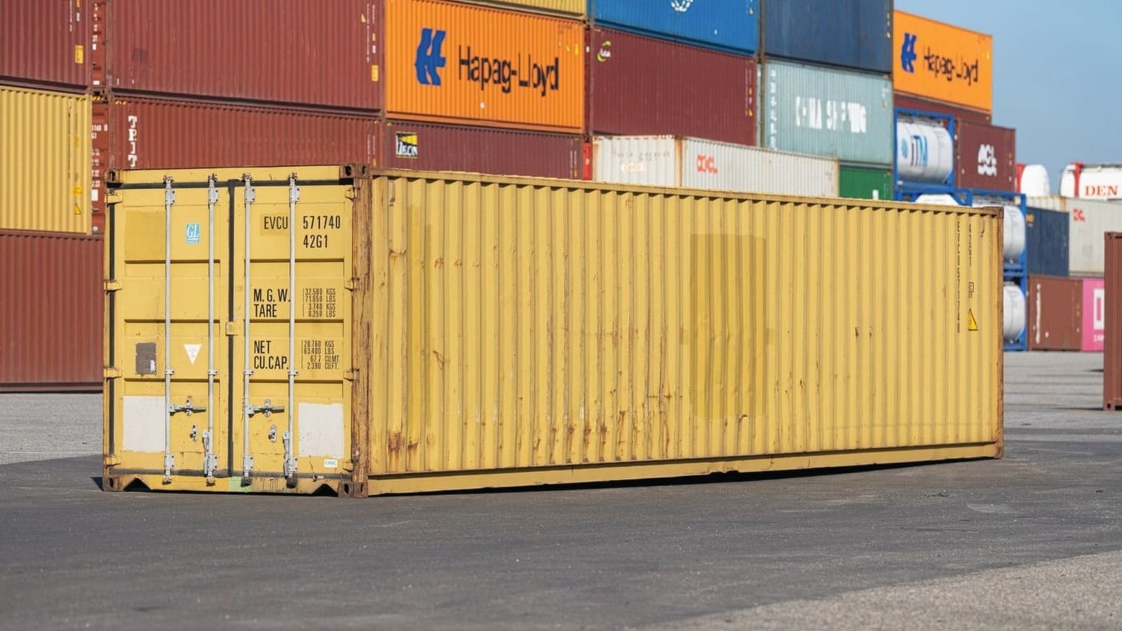 Bright yellow 40ft standard dry container standing alone at a busy shipping terminal.