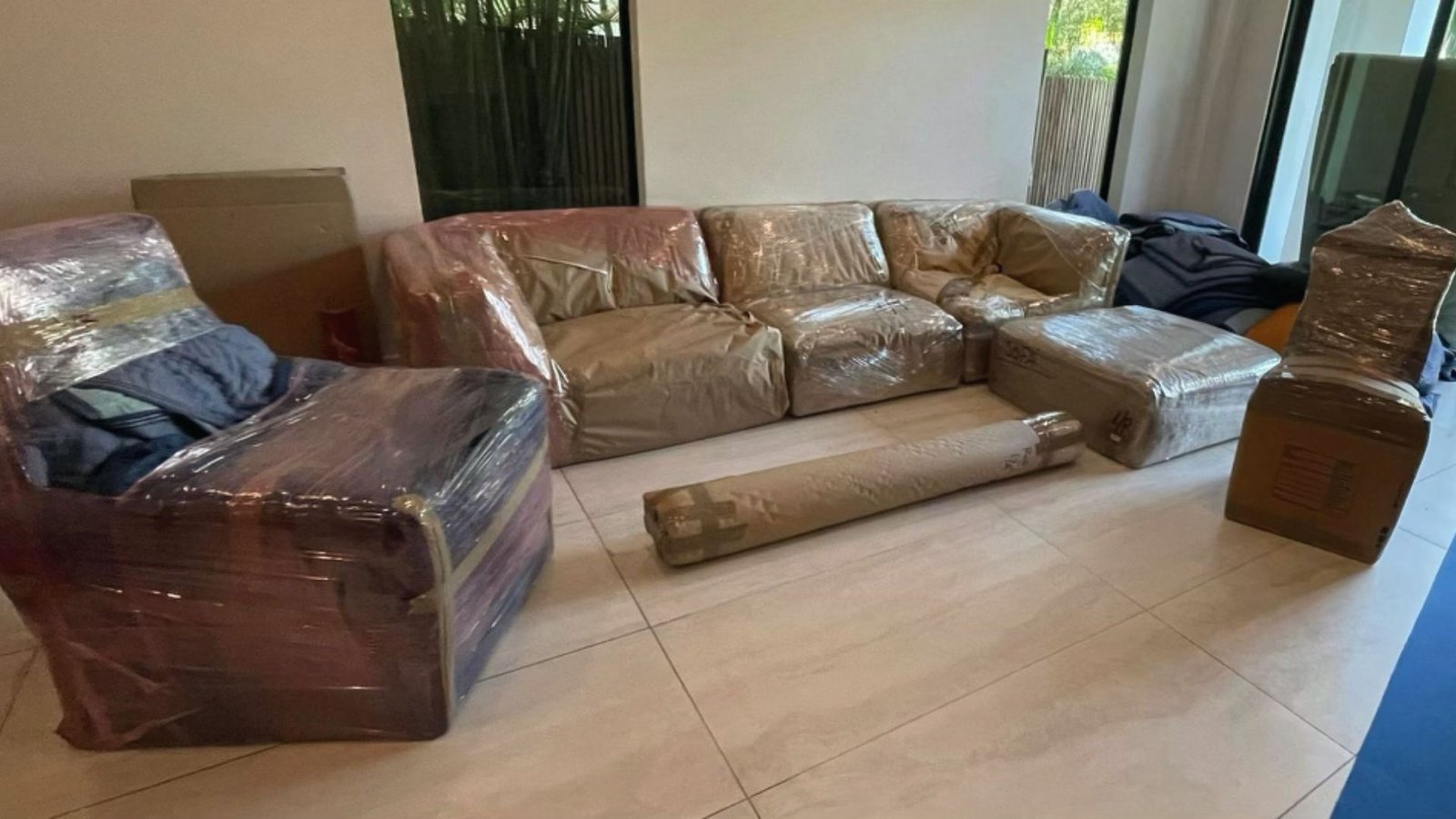 Living room with a sofa, armchairs, and ottoman fully wrapped in plastic stretch wrap for moving.