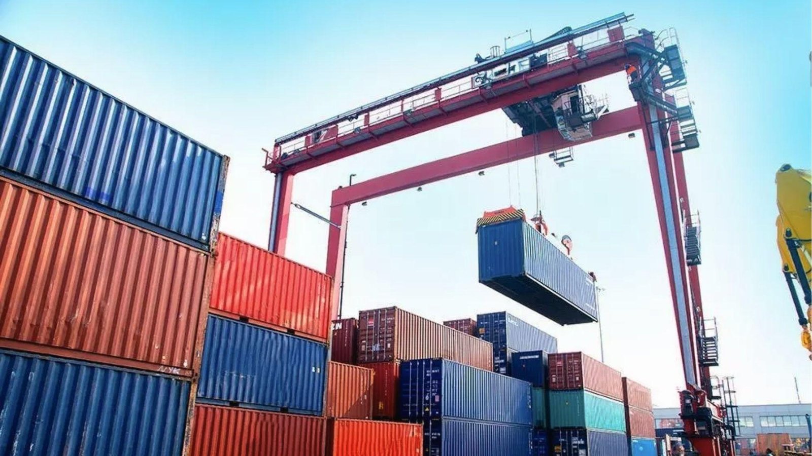 Gantry crane lifts blue container over stacked freight, highlighting port handling costs for moves.