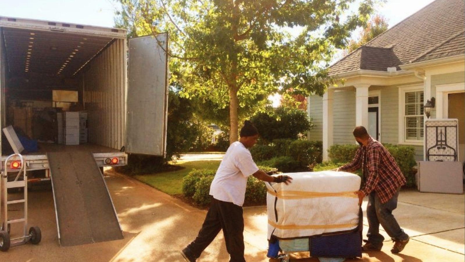 Two movers loading wrapped furniture into truck for transit to storage when move-in dates are delayed
