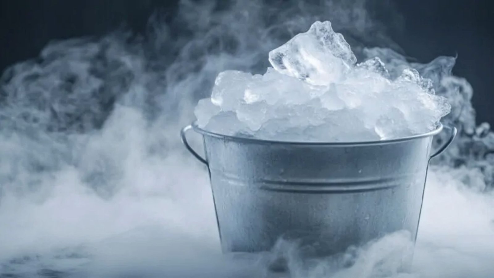 Dry ice chunks releasing dense fog from a metal bucket surrounded by vapor.