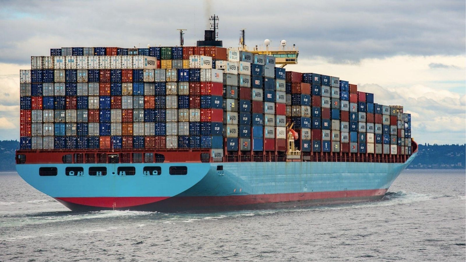 Aerial shot of a loaded container ship cutting through water, revealing thousands of TEUs aboard.